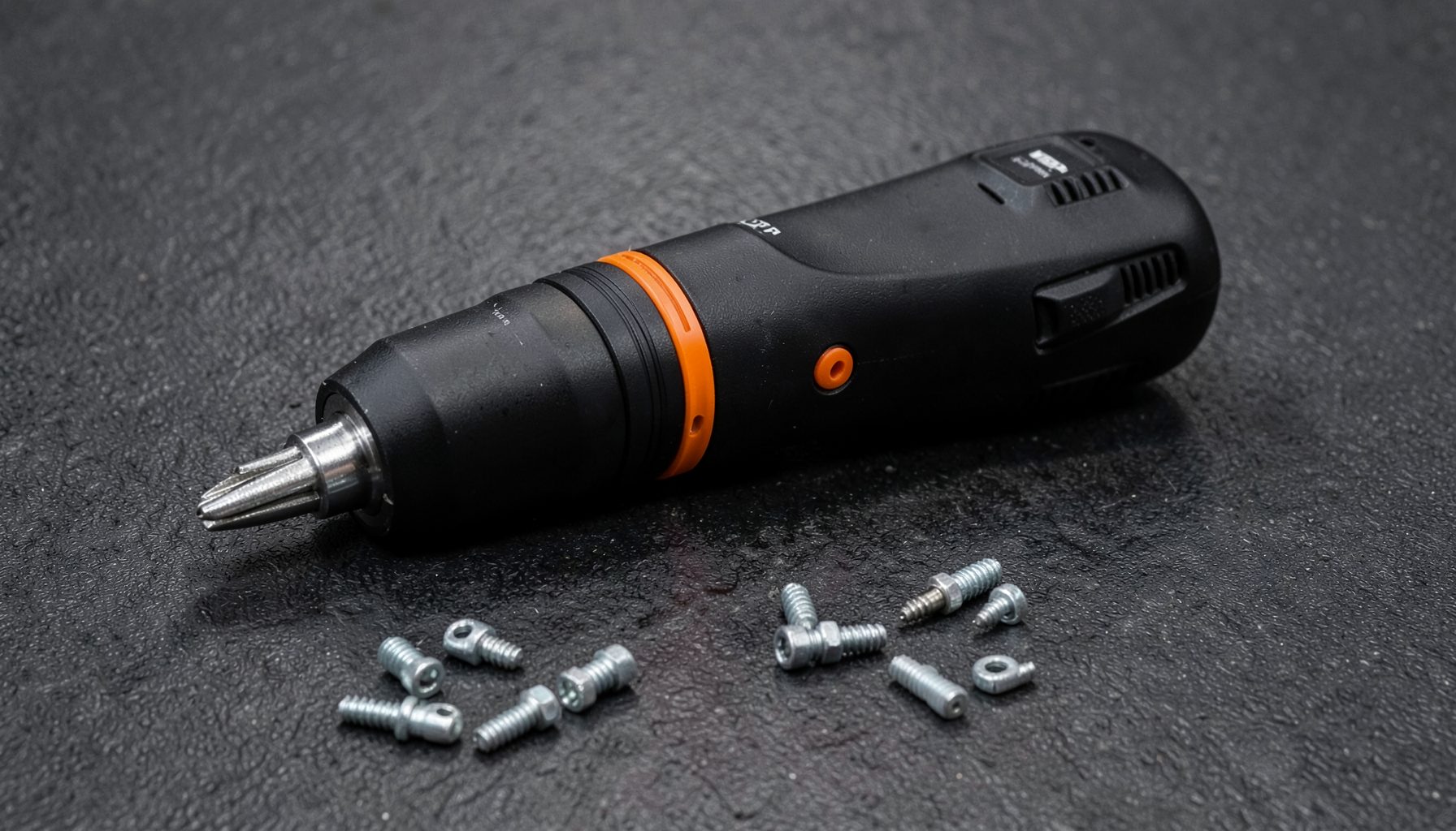 A professional-grade electric screwdriver with an orange accent ring resting on a dark textured surface beside scattered fasteners