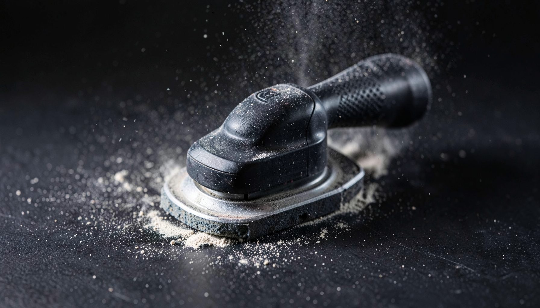 An orbital sander on a dark surface with fine dust particles catching the light